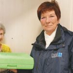 Fahrerin von Essen auf Rädern übergibt Menüschale an Seniorin