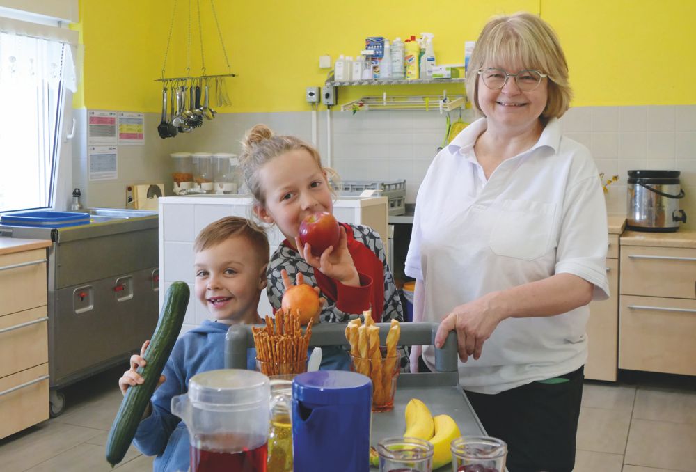 Mitarbeiterin Kita-Küche mit Kindern am Essenwagen